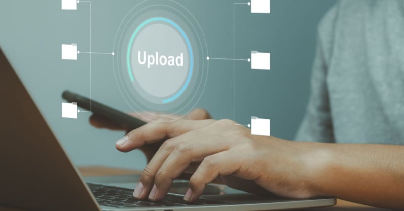 Close-up of a person using a laptop and smartphone, with a digital upload icon and folder graphics representing secure file sharing in a client portal.