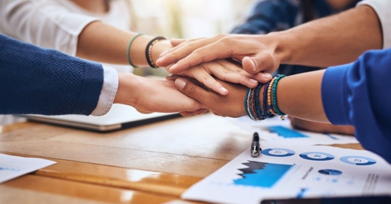 A close-up of multiple hands stacked together in a gesture of unity, teamwork, and support. 