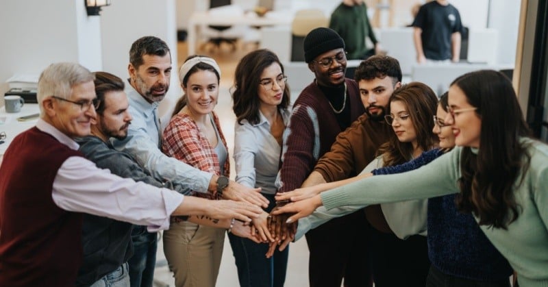 Coworkers leaning in to join hands in an office setting signifying diverse company culture