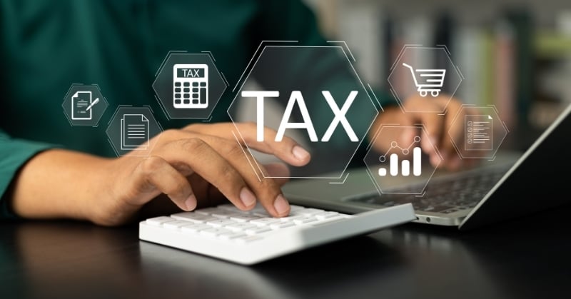 Person using a calculator beside a laptop with digital tax, shopping cart, document, and analytics icons.