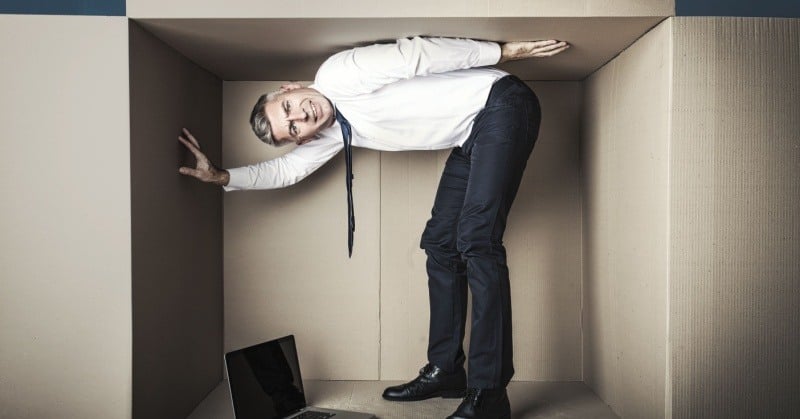 Businessman in a cramped box, symbolizing limited growth space and professional constraints.