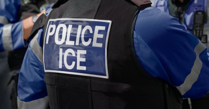 Back of an ICE officer wearing a vest labeled “POLICE ICE” during an enforcement operation.