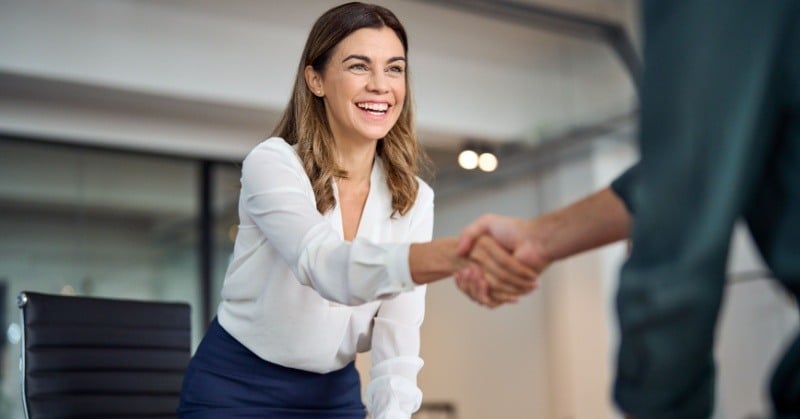 Young professional leaning over her desk to shake hands with a potential client