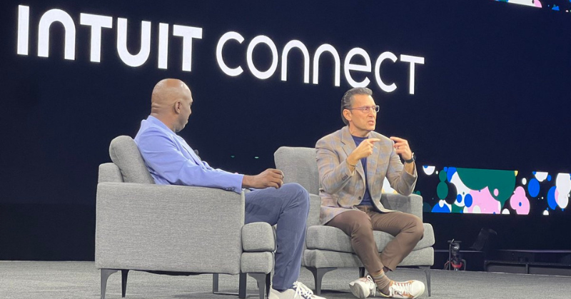 Intuit CEO Sasan Goodarzi and Chief Commercial Officer Greg Johnson engage in a fireside chat on stage at Intuit Connect 2024. The two are seated in gray chairs with the Intuit Connect logo illuminated behind them. Photo attribution: Nicole Davis