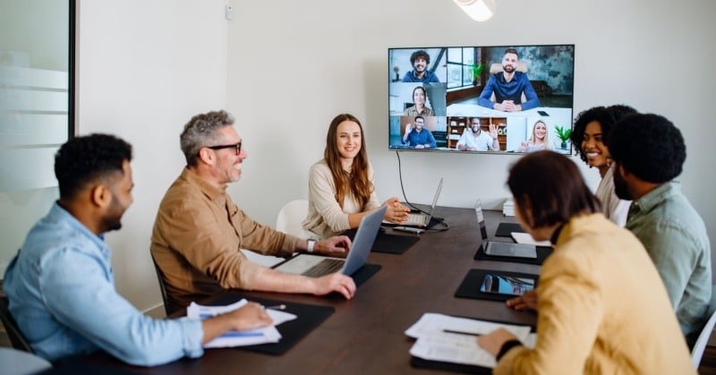 Tech savvy team collaborating around a conference table while meeting with remote team members