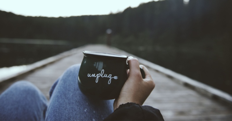 Person leaning back on the open road with a black mug with the word "unplug"