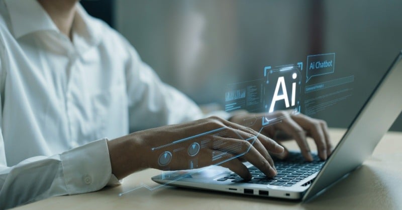 A person typing on a laptop, with holographic AI icons and chatbot graphics floating above the keyboard, representing artificial intelligence technology and digital interaction. The image conveys the concept of working with AI tools and automation.