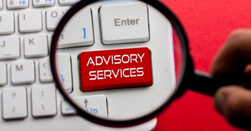 A magnifying glass highlighting a red keyboard key labeled 'Advisory Services' on a white keyboard, symbolizing the focus on professional consulting.