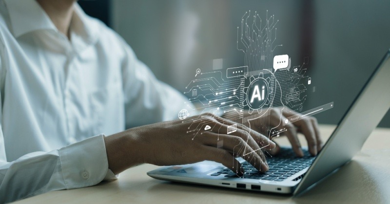 artificial intelligence AI white hologram graphics floating above laptop keyboard as person whose face cannot be seen types on it at a light colored desk