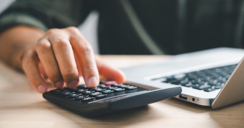 Hand on calculator, laptop on desk, dark shirt, human hand, pricing models