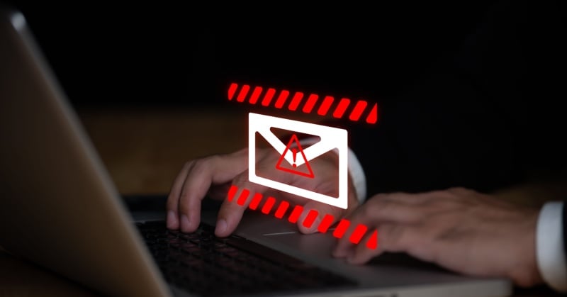 red and whtie hologram depicting email symbol hovering above laptop with hands with dark suit jacket and white shirt on keyboard 