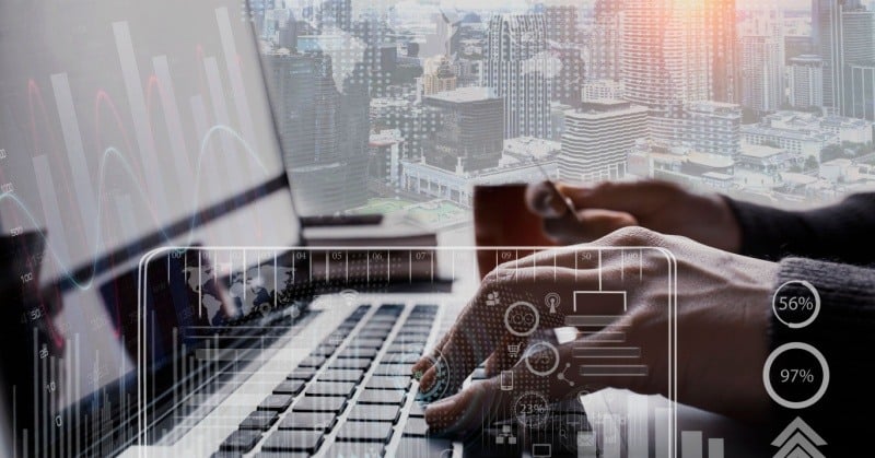 fingers on laptop keyboard against a city skyline backdrop with white transparent symbols overlayed in foreground of image