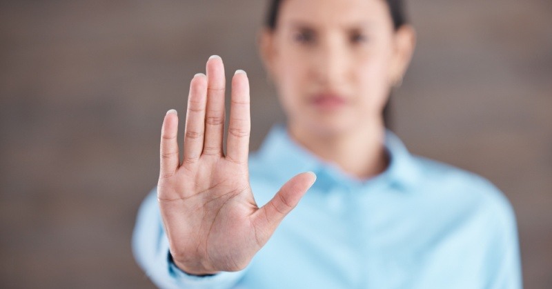 woman with dark hair and light blue shirt holding hand up stop gesture