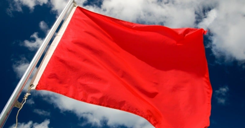 Red flag waving against cloudy blue sky