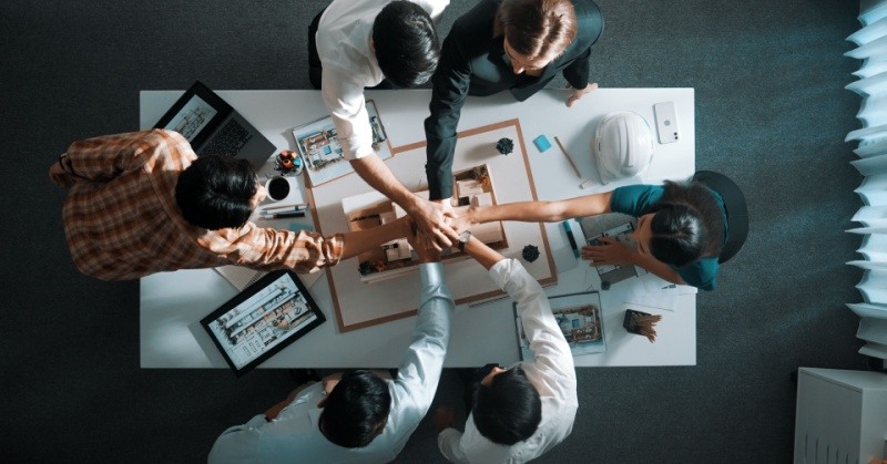 top-down view of diverse team of six sitting at white conference table with hands in center