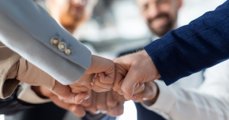 multiple human fists bumping in a circle blue and grey business attire networking