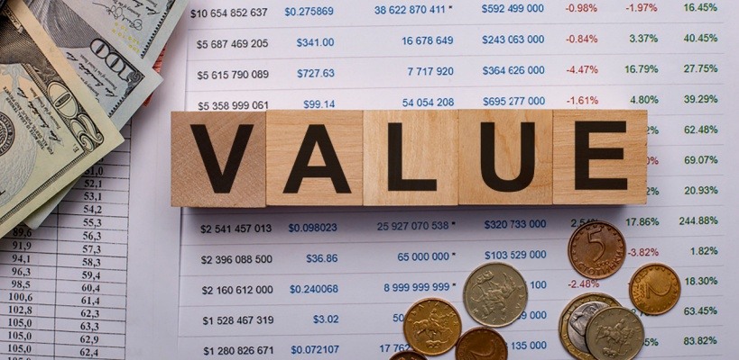 wood blocks with black letters spelling out value atop spreadsheet with money multiple denominations in background